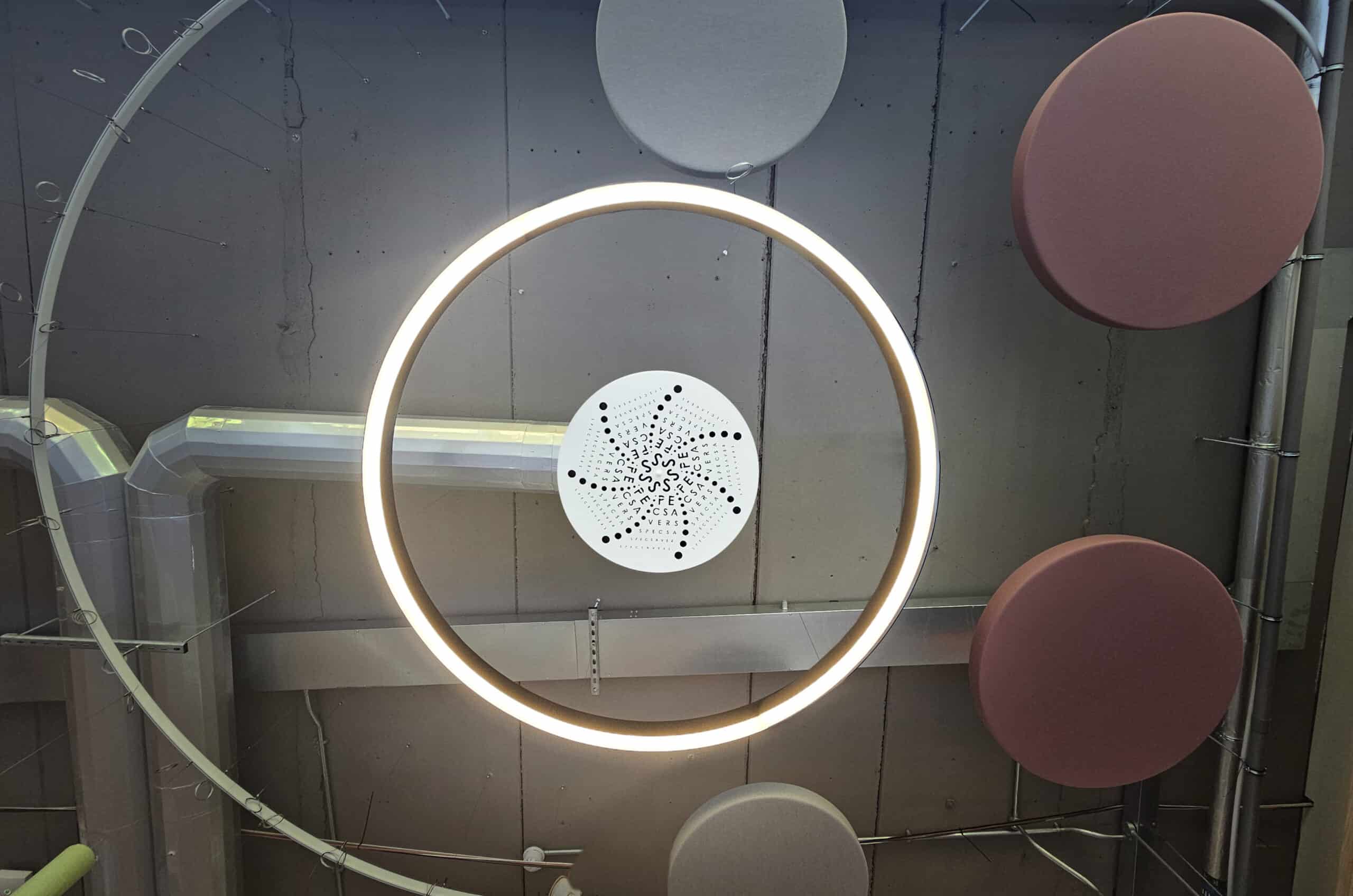 Specsavers' logo cut into a swirl diffuser, fitted into an exposed ceiling with a ring LED around it.